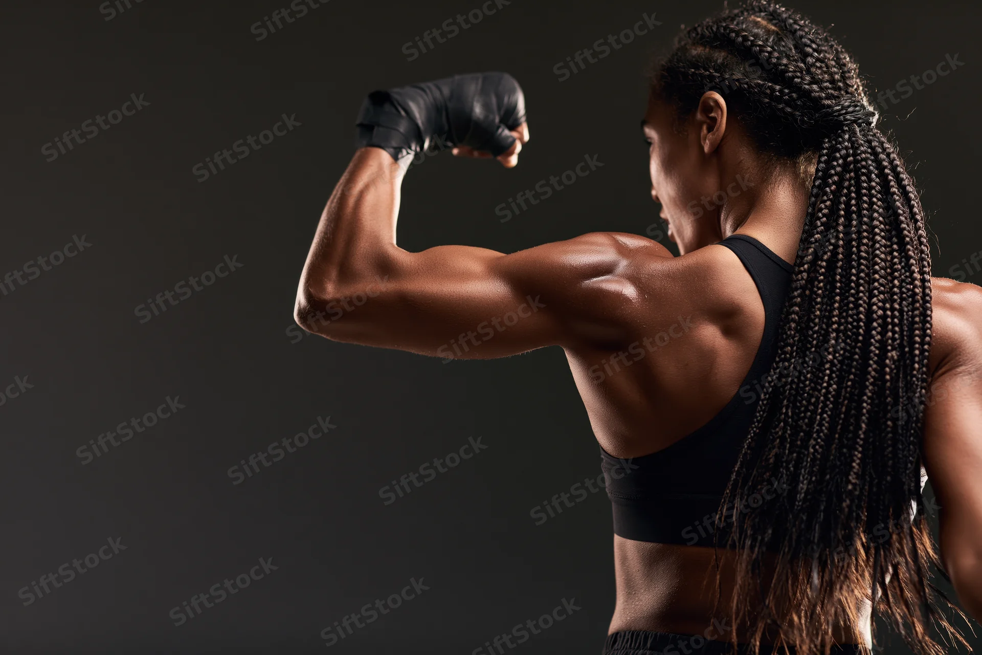 Black woman boxer flexing bicep in profile against dark studio background