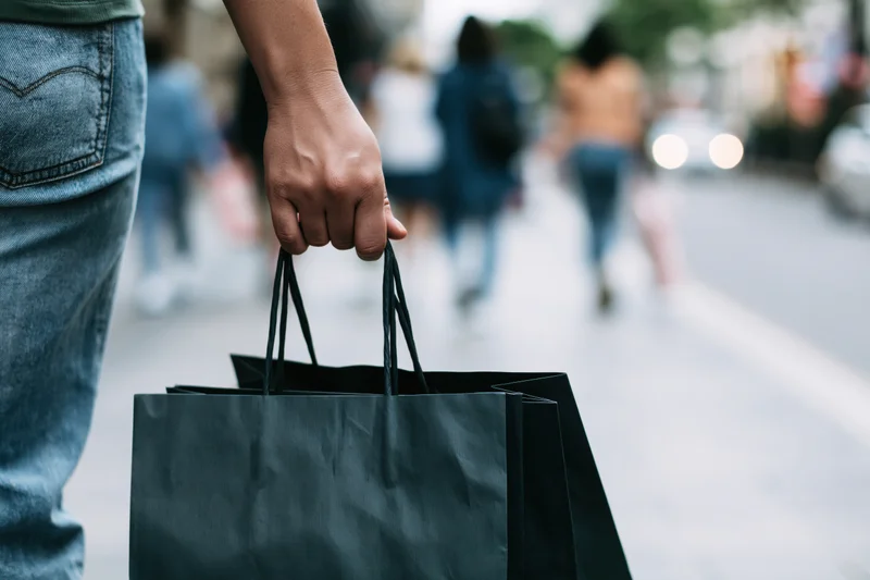 Woman's hand holding black paper shopping bags on city sidewalk