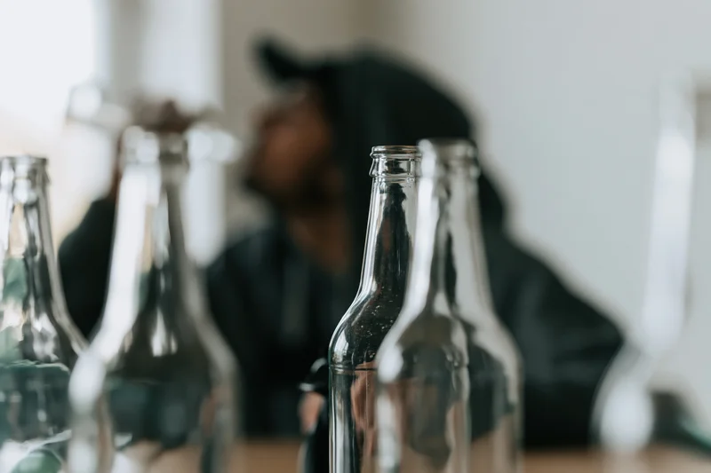 Empty glass bottles in sharp focus on a table with a blurred man in a hoodie in the background