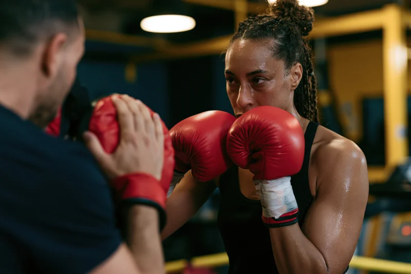 Female boxer in defensive stance with red gloves up guarding in a gym