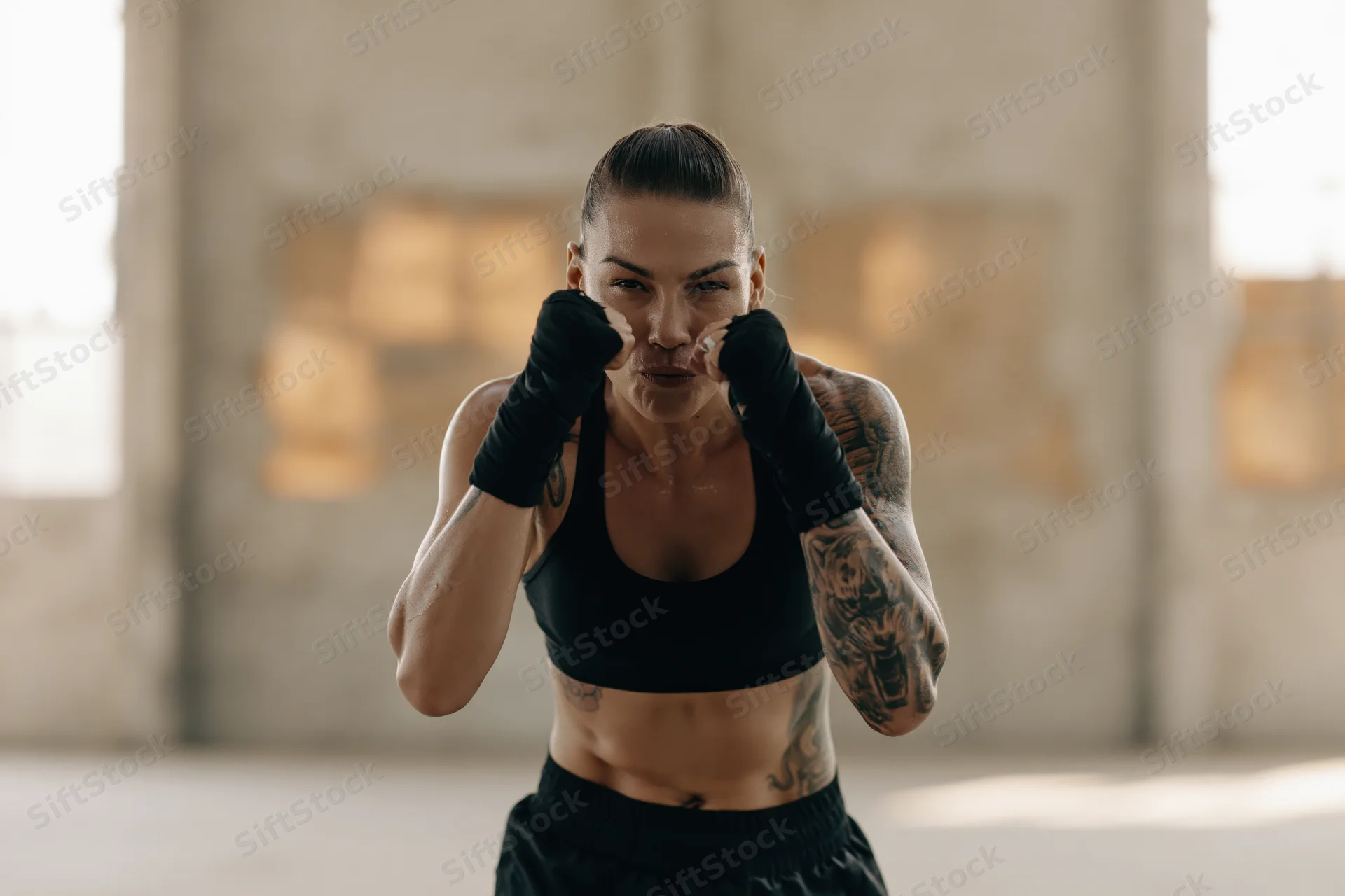 Woman in fighting stance with fists raised guarding her face in an indoor training space