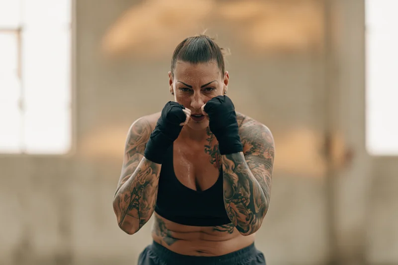 Woman in fighting stance with fists raised guarding her face in a gym