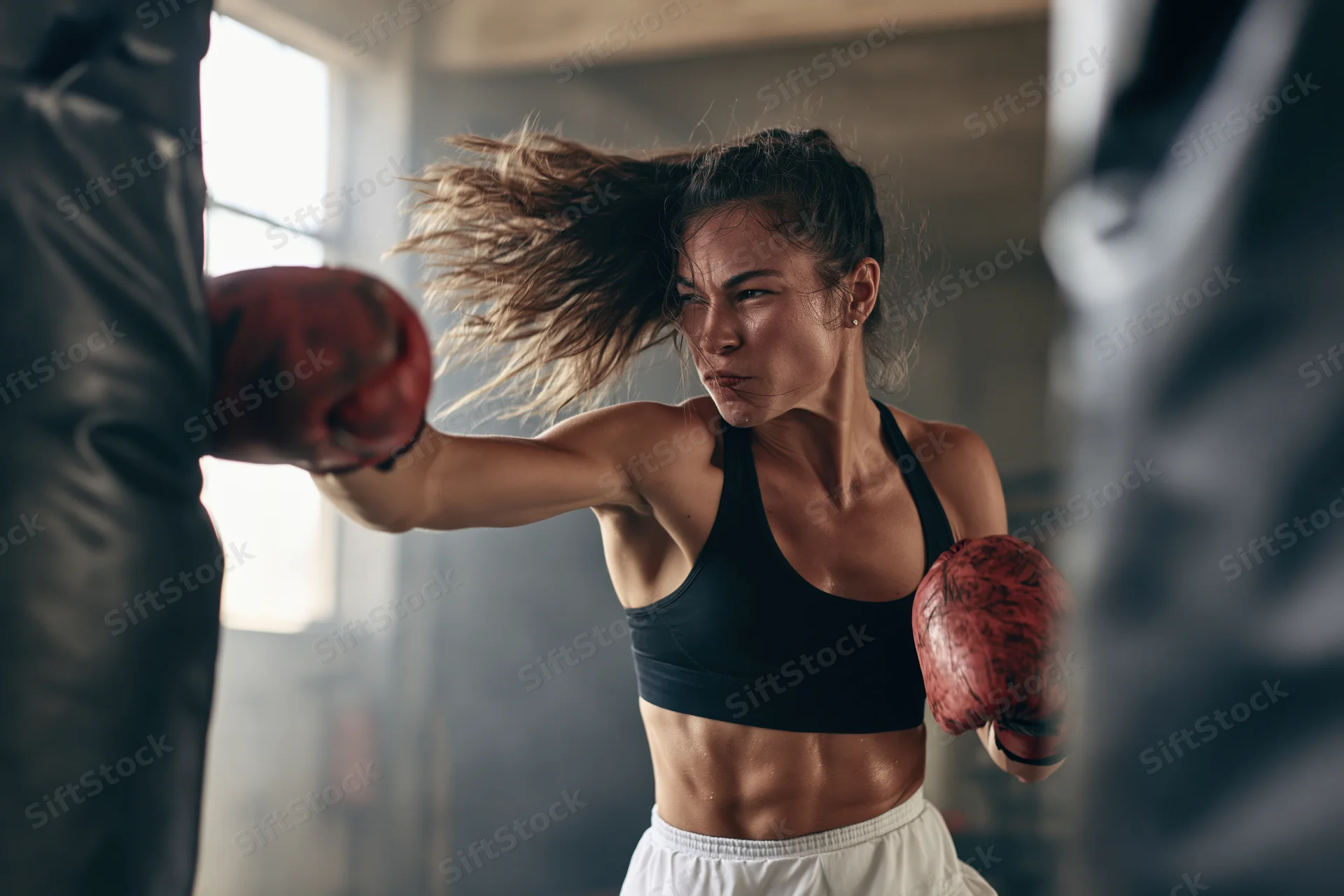 Woman boxer mid-punch striking a heavy black punching bag in a gym