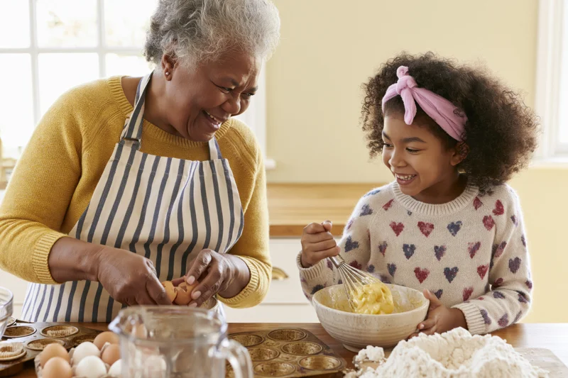 Grandmother and granddaughter baking together in a kitchen, smiling as they mix ingredients and prepare muffins