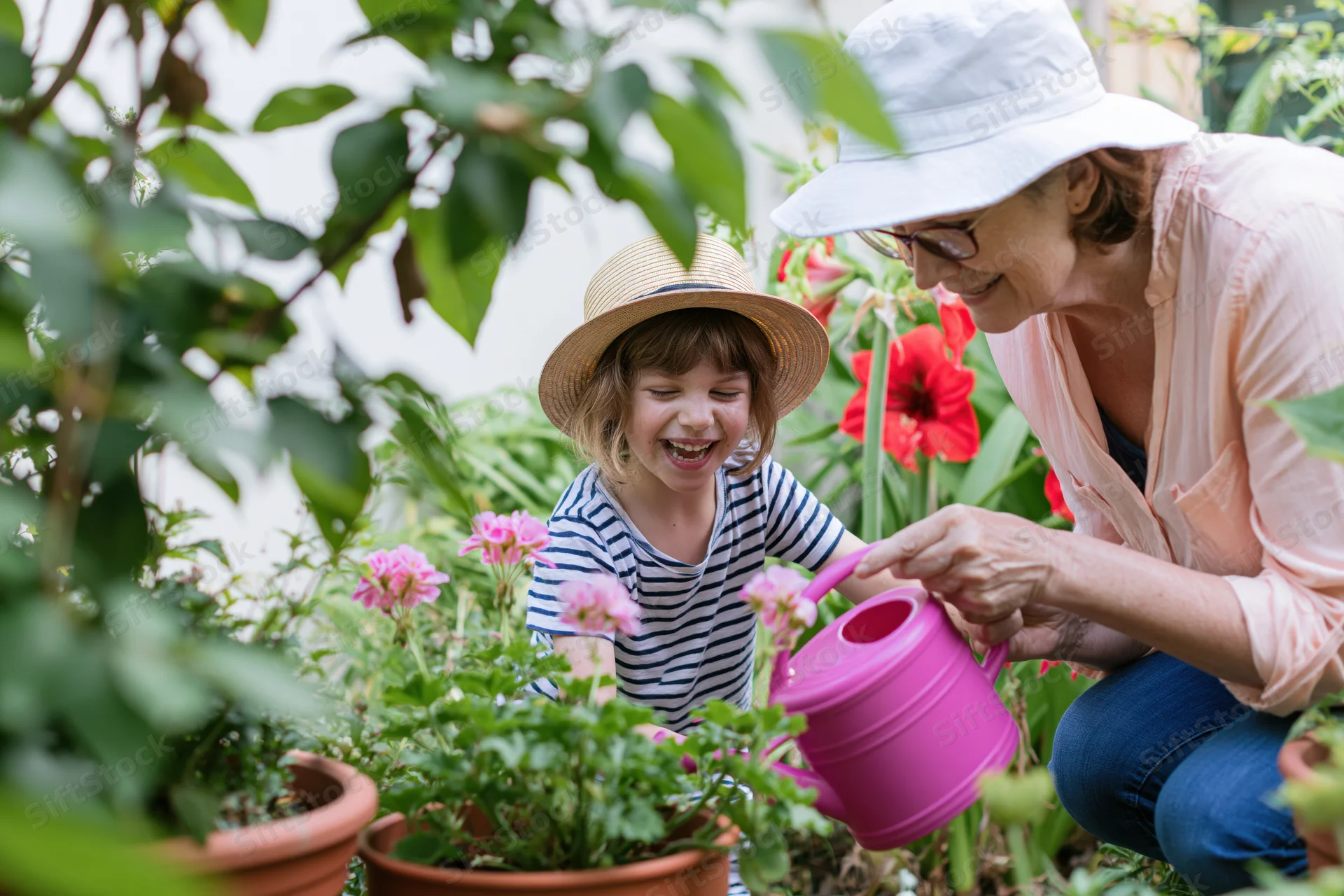 Grandmother and granddaughter watering potted flowers in a garden