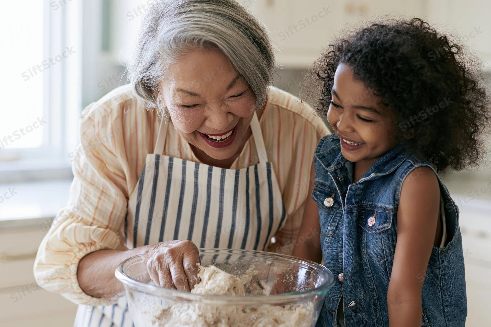 Grandmother and child laughing while mixing dough in a kitchen bowl