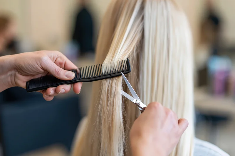 Hairdresser cutting blonde hair with scissors and comb in salon