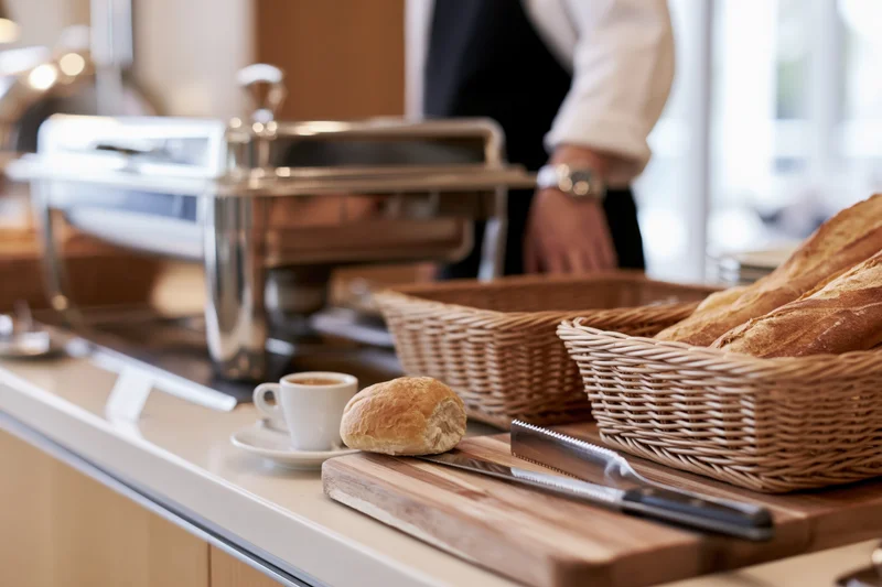 Breakfast buffet counter with bread in wicker baskets and coffee cup on wooden cutting board