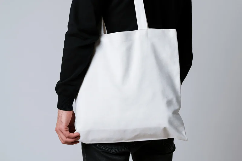Man carrying a plain white canvas tote bag over his shoulder in a studio setting