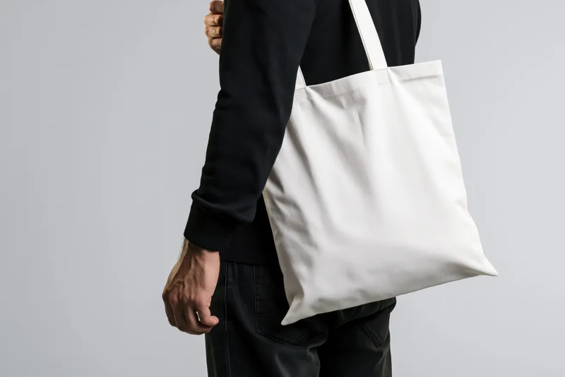 Man carrying plain white canvas tote bag over shoulder in studio setting