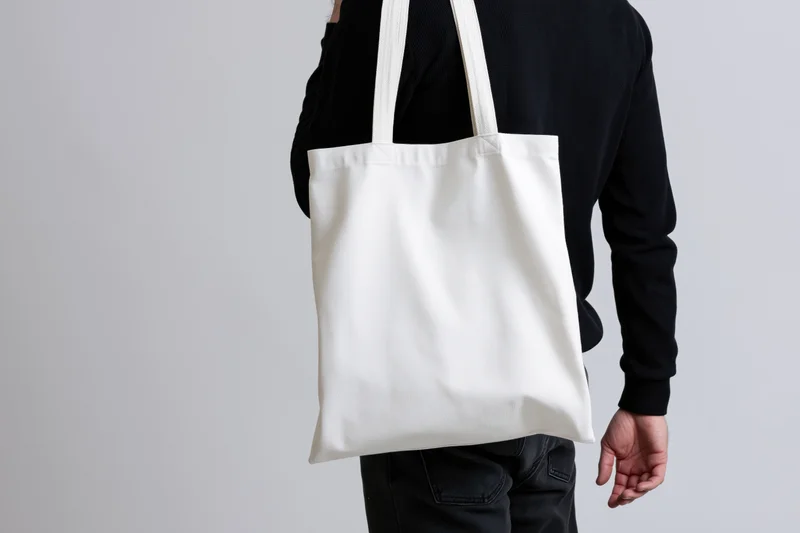 Man carrying a blank white canvas tote bag over his shoulder in a studio setting