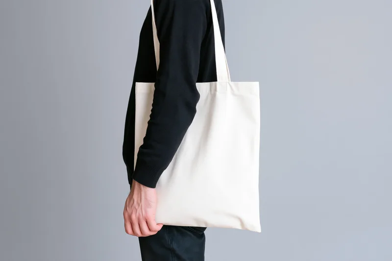 Man carrying blank white canvas tote bag over shoulder against gray background