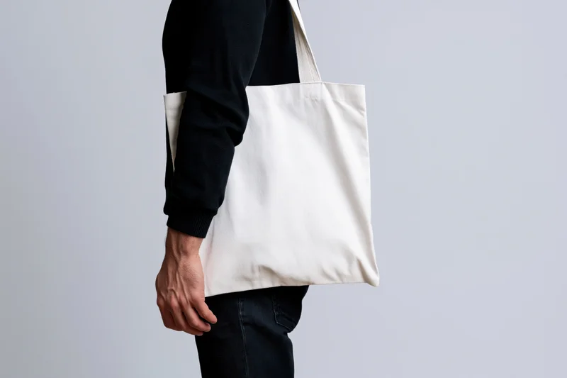 Man carrying blank white canvas tote bag over shoulder in studio setting