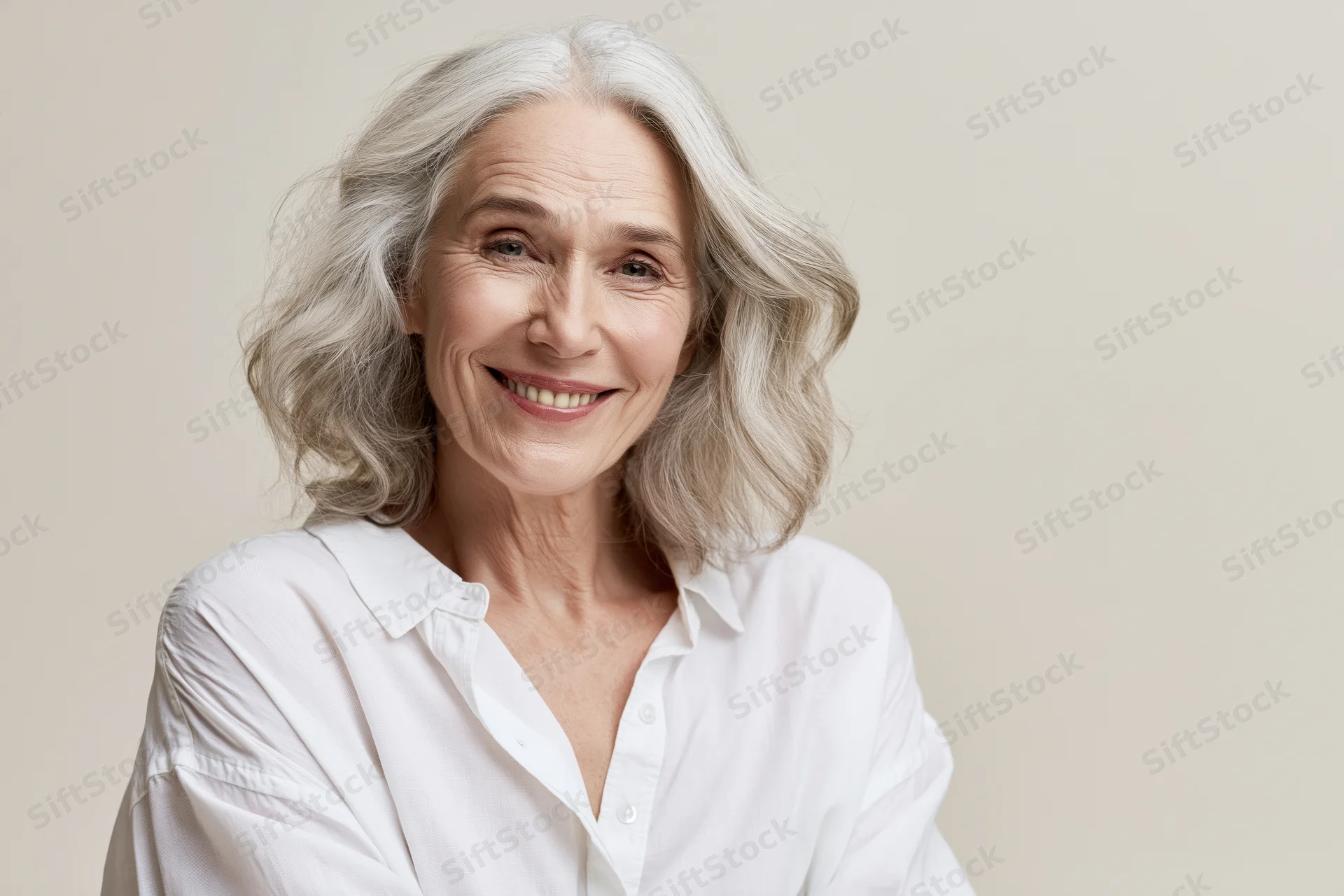 Mature woman smiling warmly at camera in white blouse against neutral background