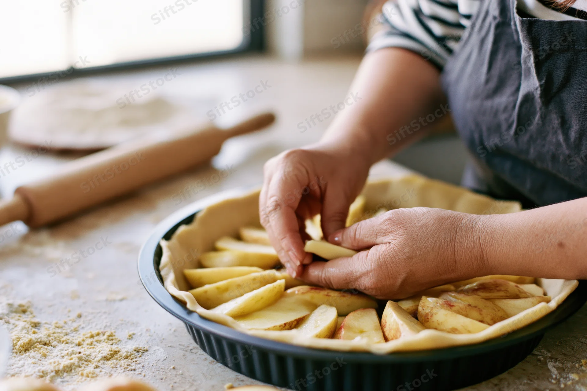 Woman arranging apple slices in a pie crust on a kitchen counter