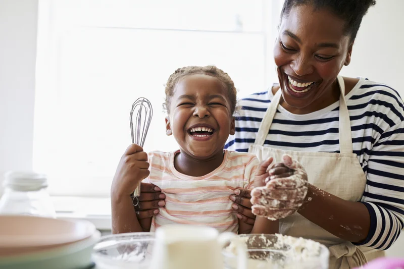 Mother and daughter laughing while baking together in a home kitchen