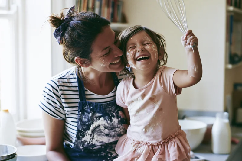 Mother and daughter laughing while baking together in kitchen