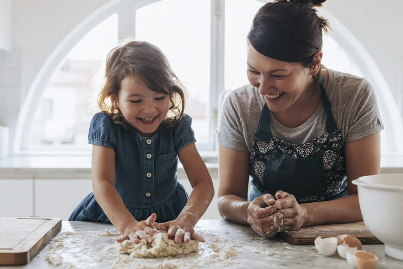Mother and daughter laughing while kneading dough on a kitchen countertop