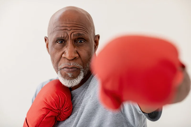 Senior black man in fighting stance throwing a jab with red boxing gloves in studio