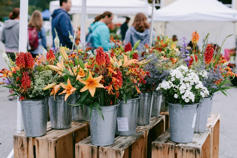 Colorful flower arrangements in galvanized metal buckets on wooden crates at outdoor farmers market