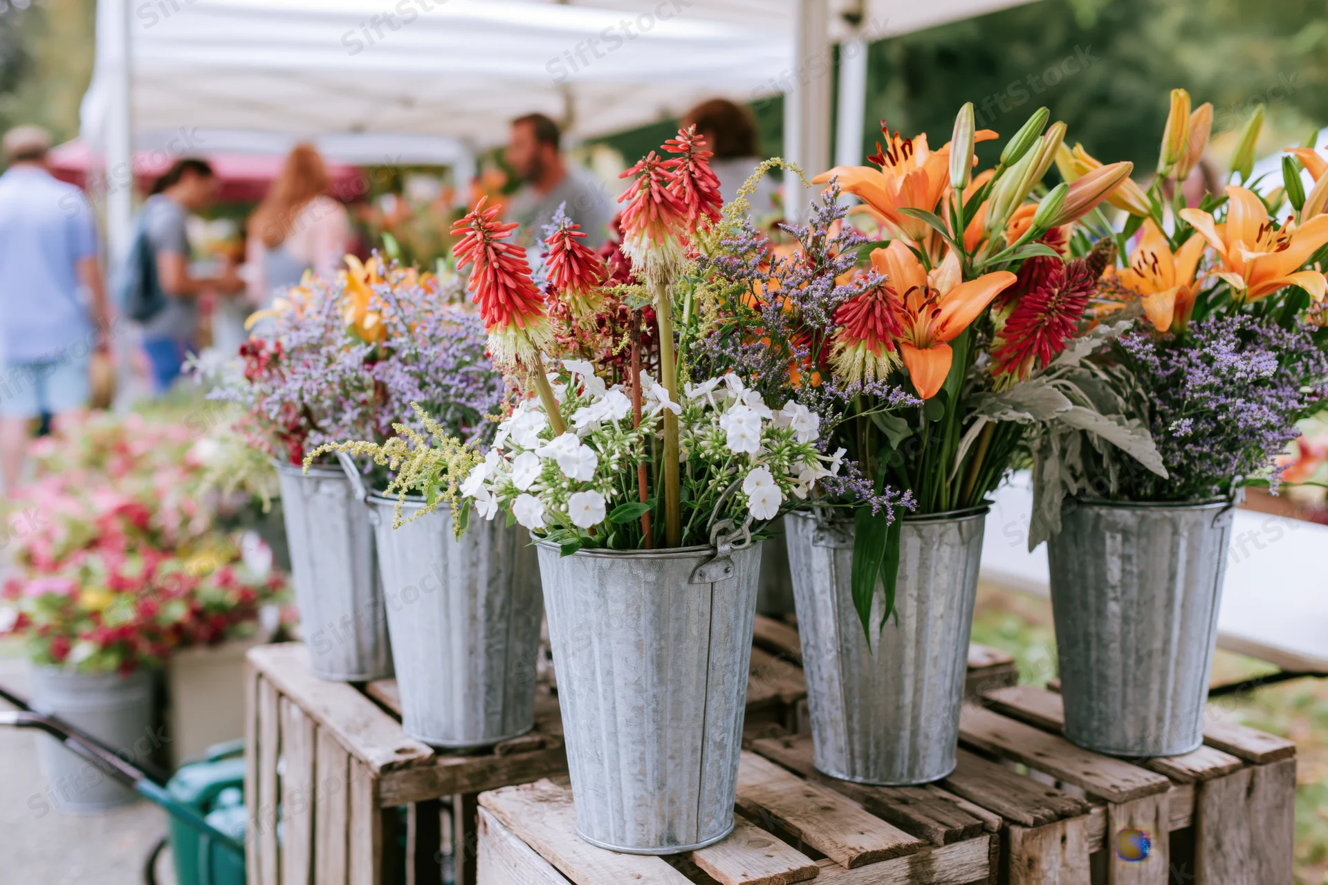 Colorful flower arrangements in galvanized metal buckets on wooden crates at outdoor market