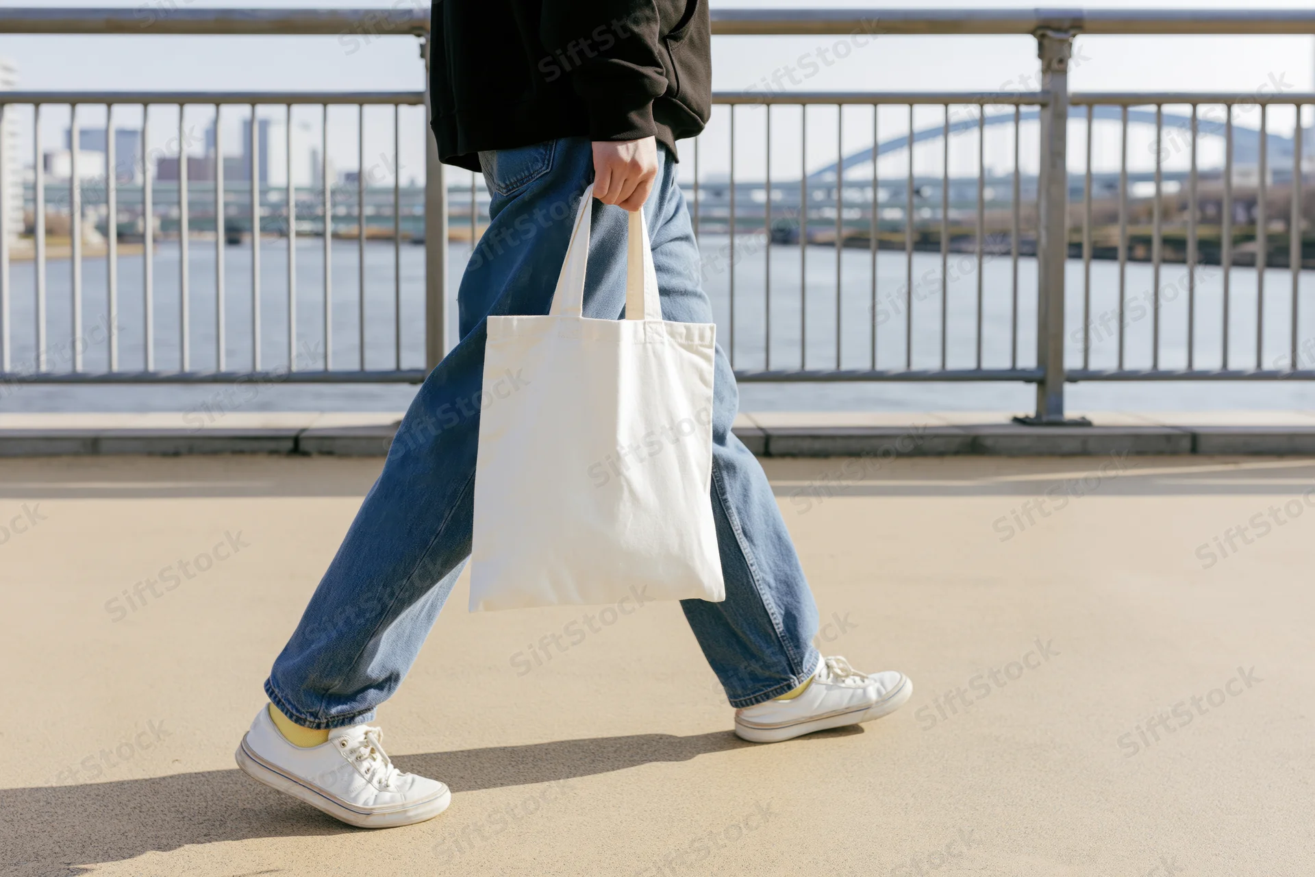 Person walking across pedestrian bridge holding plain white tote bag