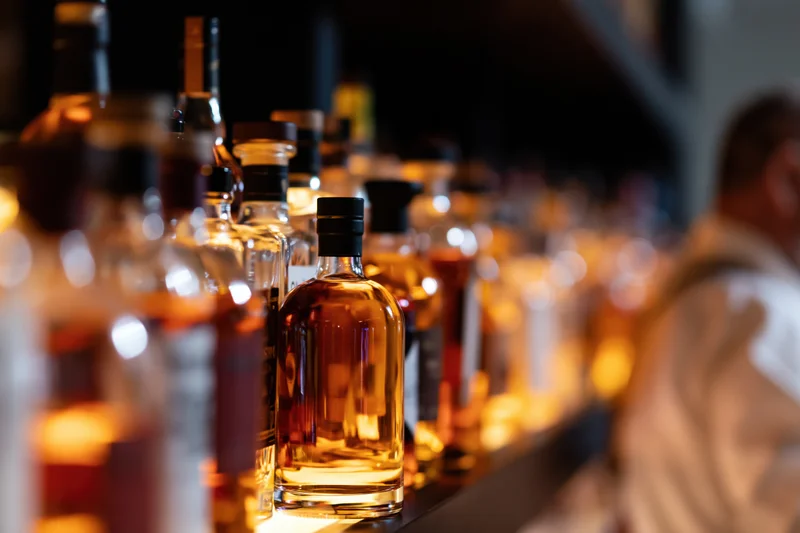 Row of whiskey bottles lined up on a backlit bar shelf with warm glow and blurred background