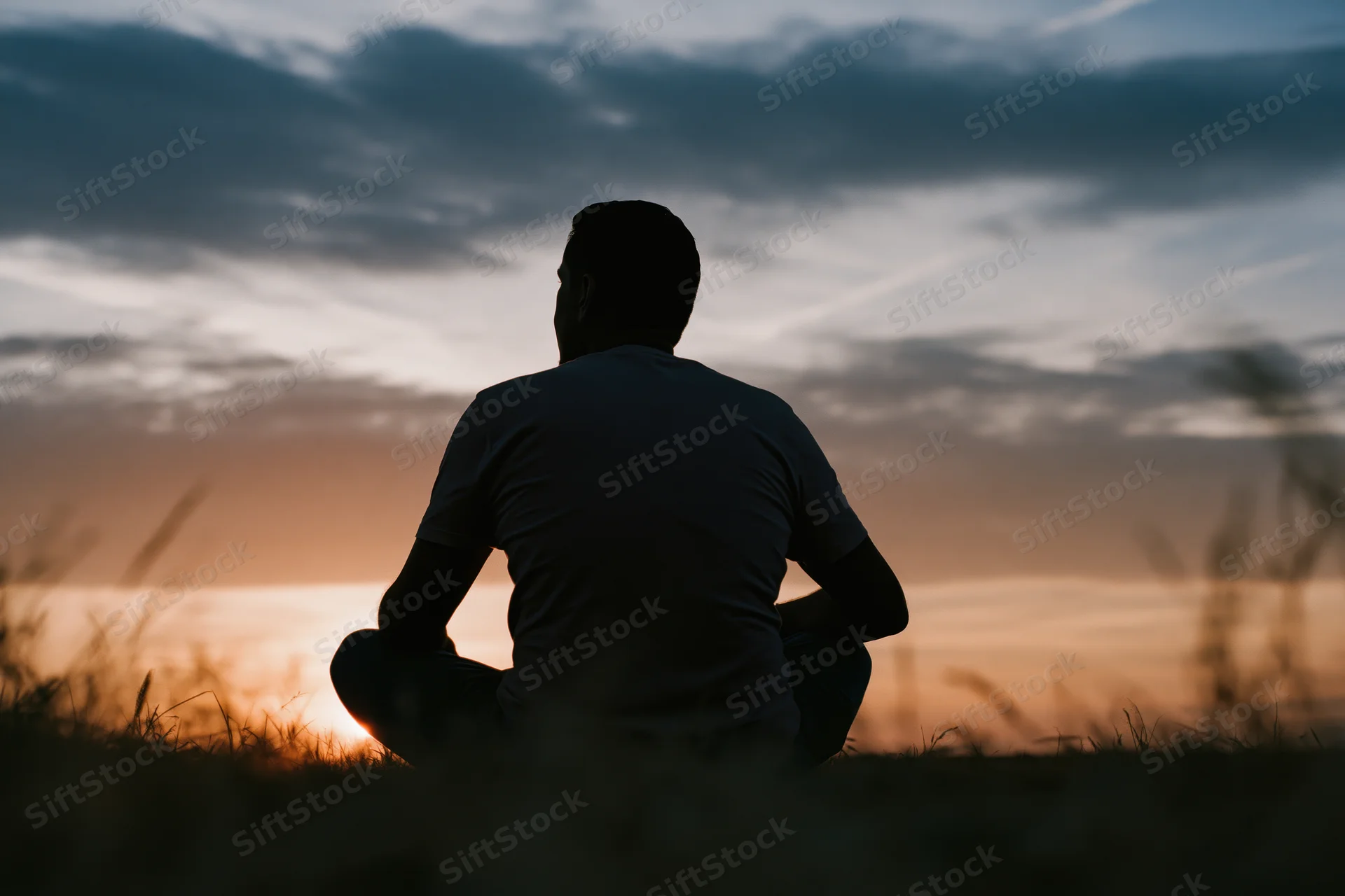 Silhouette of a man sitting crosslegged in a grass field at sunset