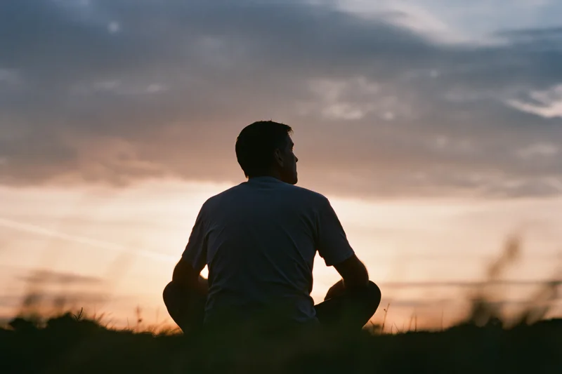 Silhouette of a man sitting alone in a grass field at sunset