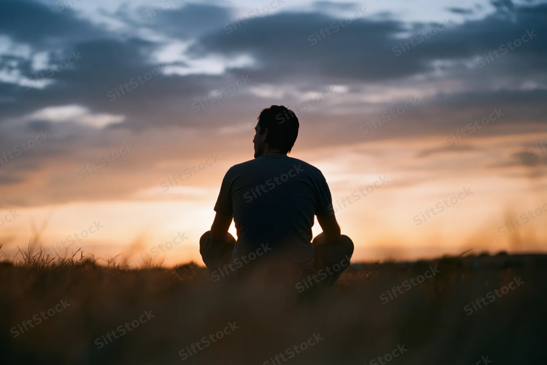 Silhouette of a man sitting cross-legged in a grass field at sunset