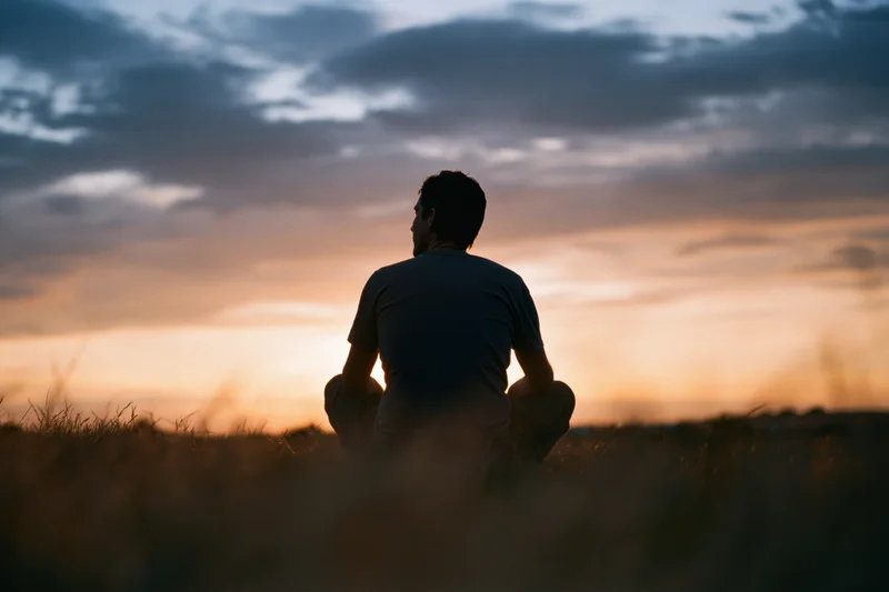 Silhouette of a man sitting cross-legged in a grass field at sunset
