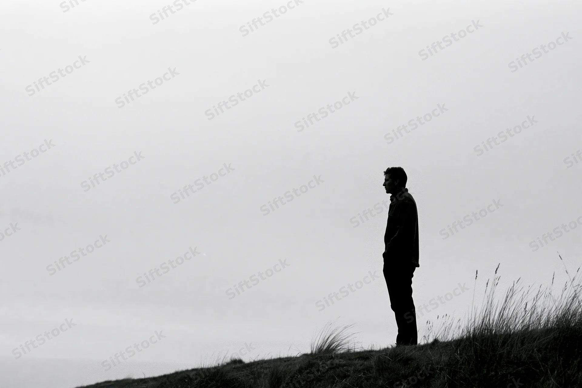 Silhouette of a man standing alone on a grassy hill under an overcast sky