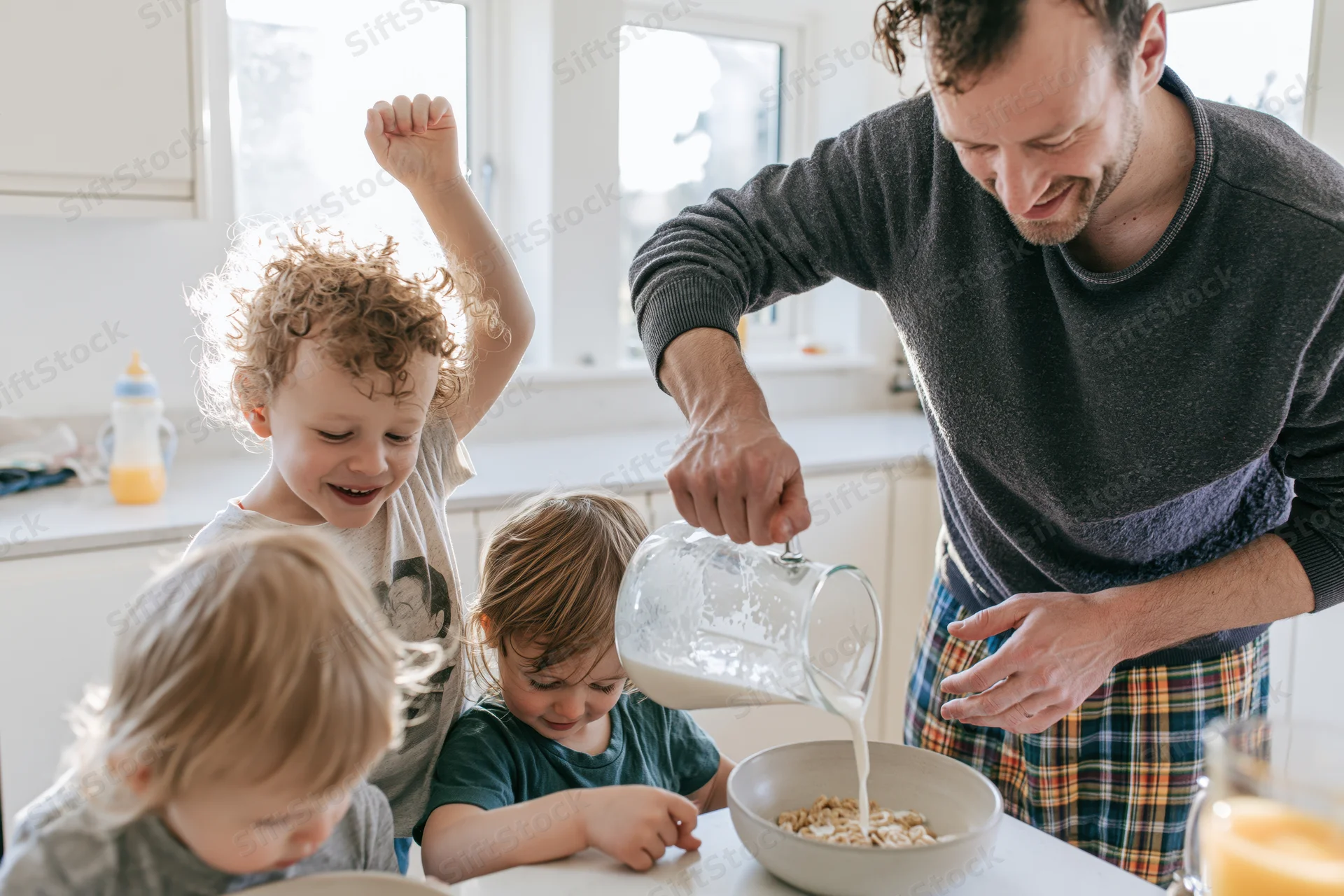 Father pouring milk into a cereal bowl while children watch in a bright kitchen