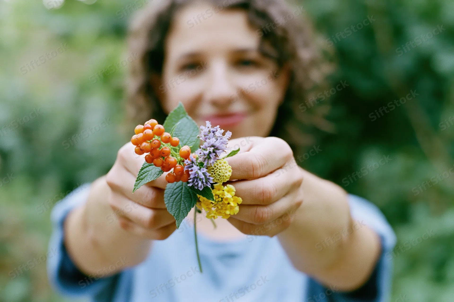 Woman holding a small wildflower with berries and leaves in a garden