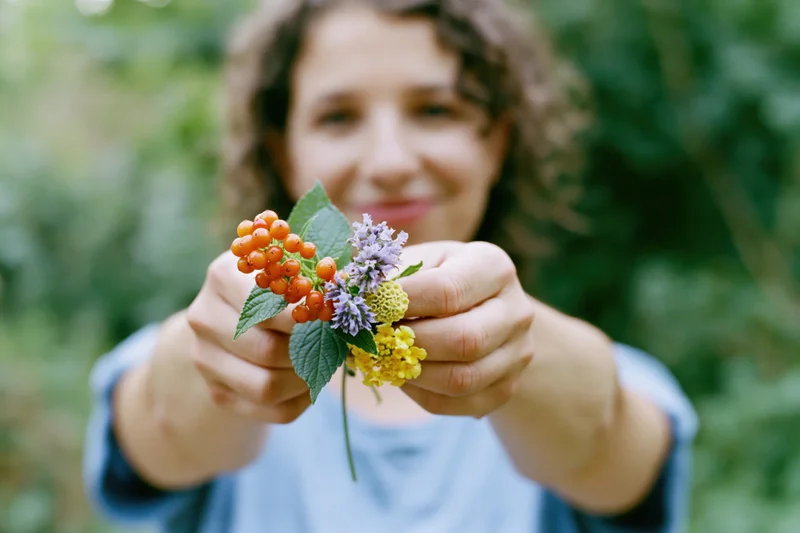 Woman holding a small wildflower with berries and leaves in a garden