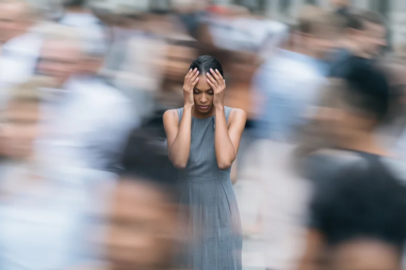 Woman holding her head in stress amidst a blurred city crowd