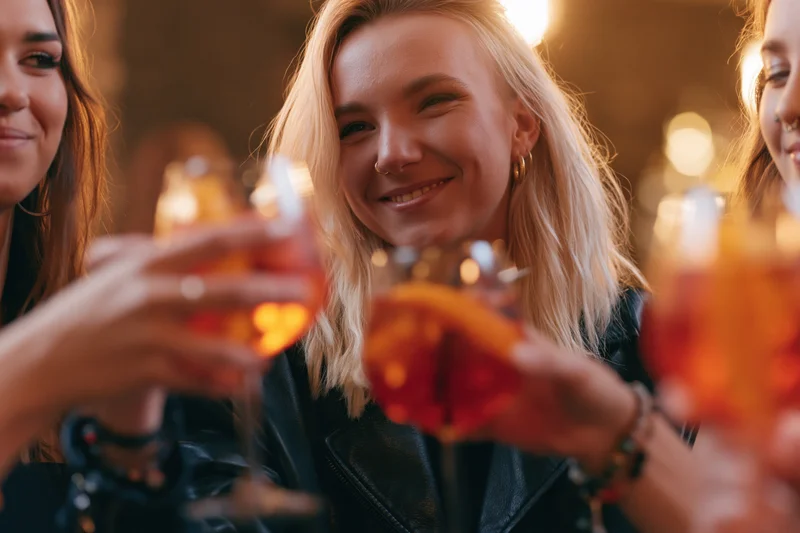 Three young women toasting with Aperol Spritz cocktails in a bar