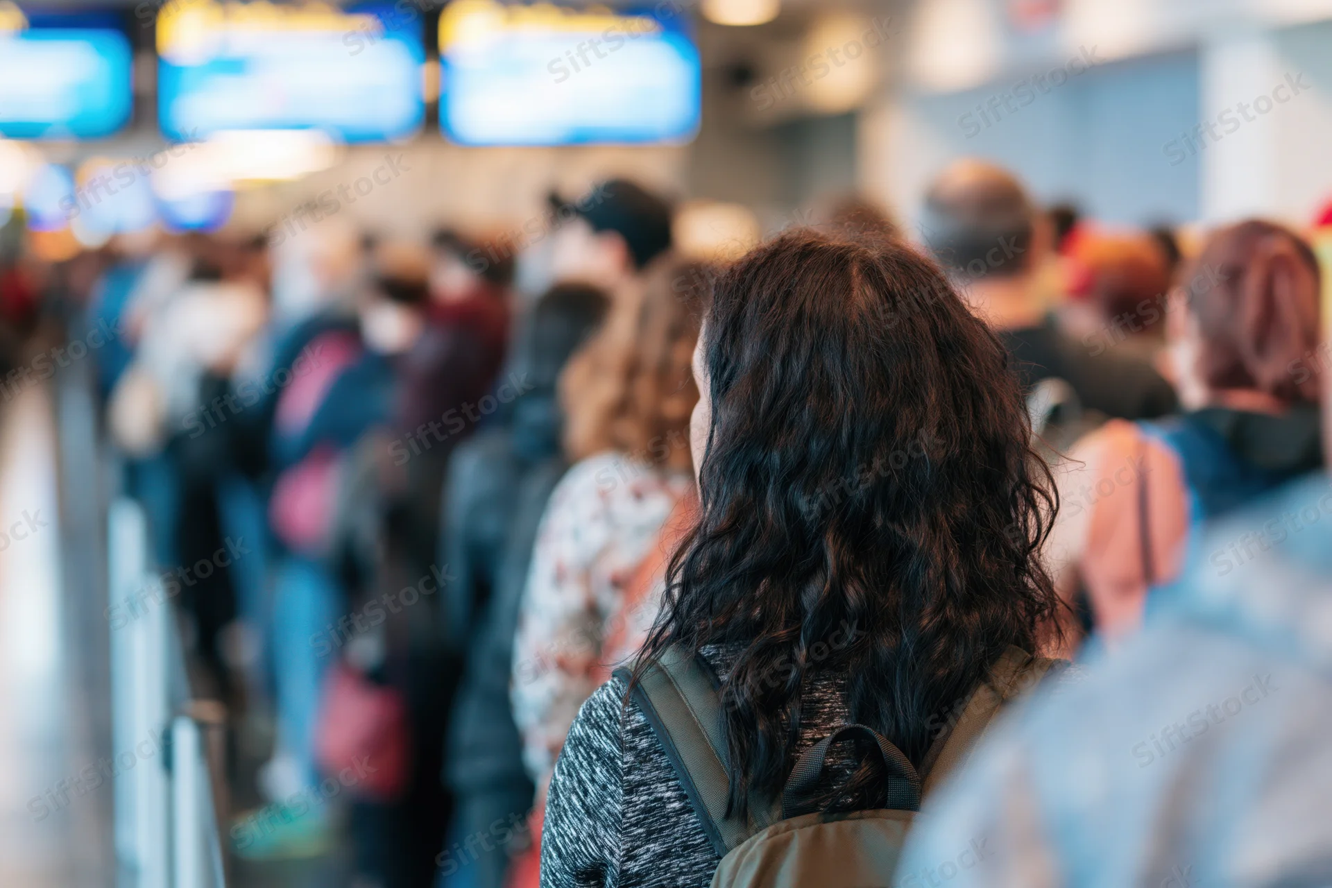 Woman with curly dark hair and backpack waiting in a long queue at airport security line