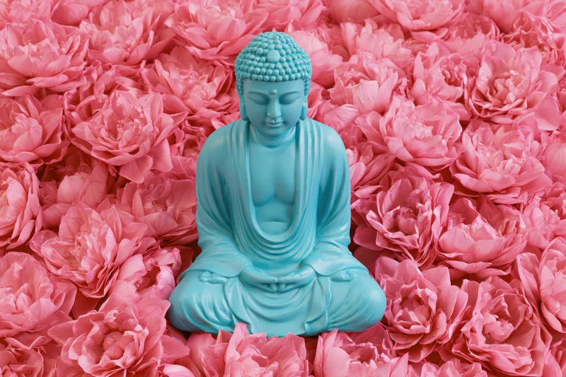 Turquoise buddha statue in seated meditation pose surrounded by pink peonies