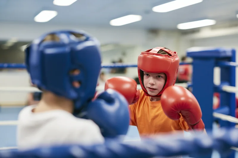 Two boys sparring in a boxing ring wearing protective gear and gloves