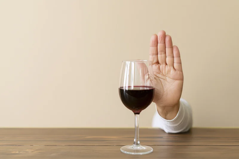 Woman raising hand in refusal beside glass of red wine on wooden table