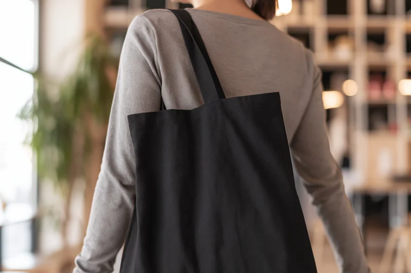 Woman from behind carrying black canvas tote bag in modern cafe interior