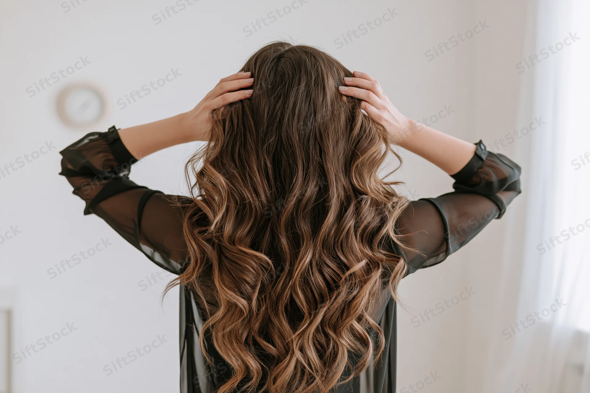 Woman from behind running hands through long wavy hair in a bright room