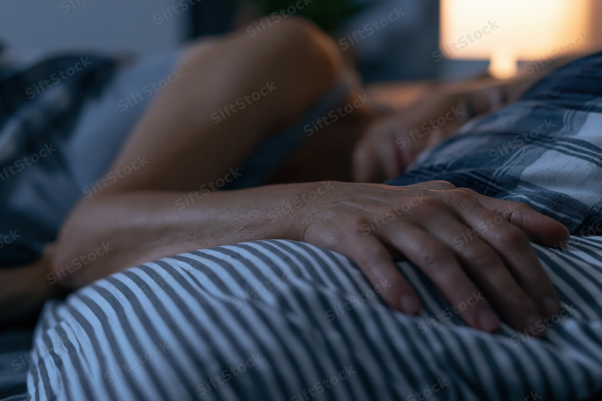 Woman sleeping peacefully in bed at night with hand resting on partner's stomach