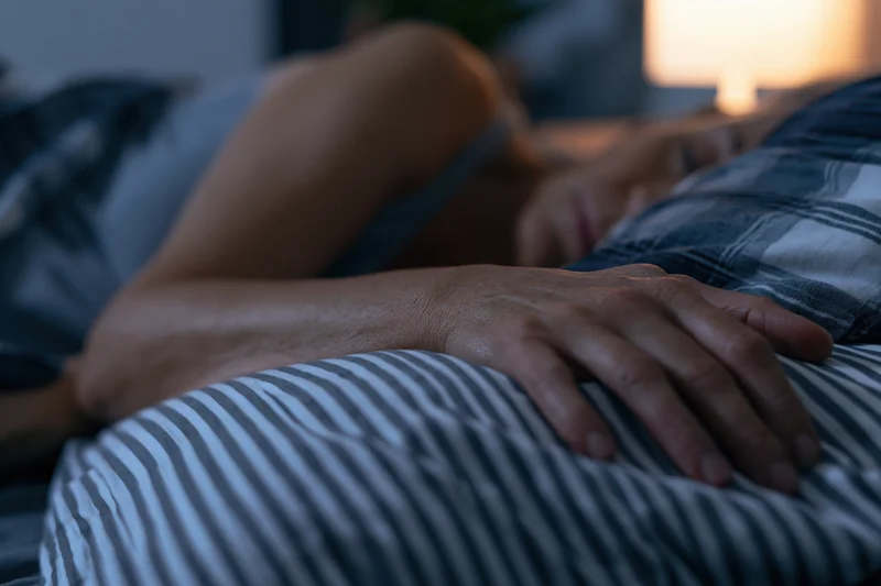 Woman sleeping peacefully in bed at night with hand resting on partner's stomach