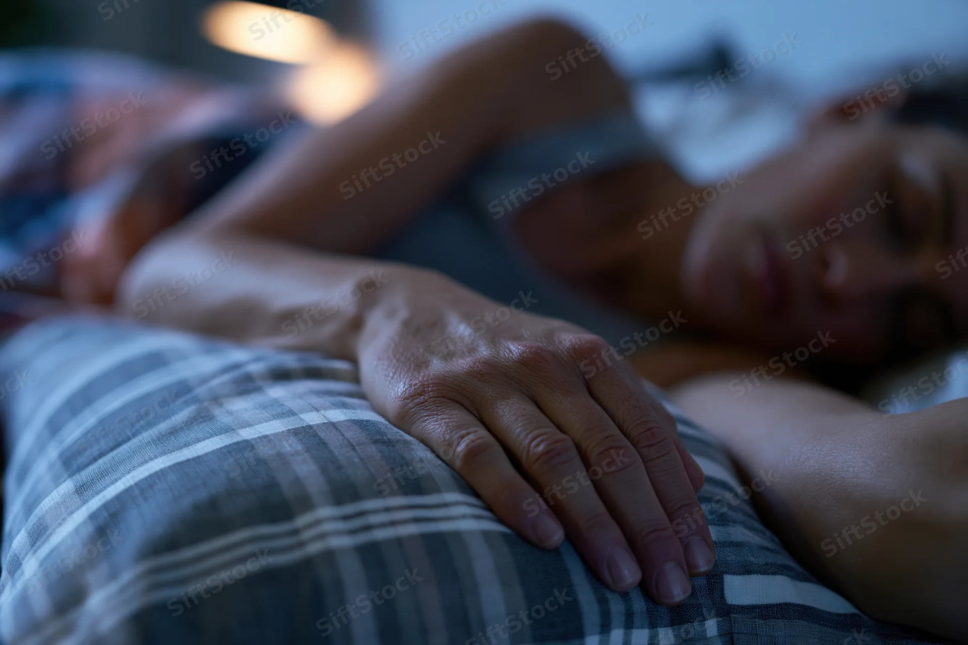 Woman sleeping peacefully in bed at night with hand resting on a plaid pillow