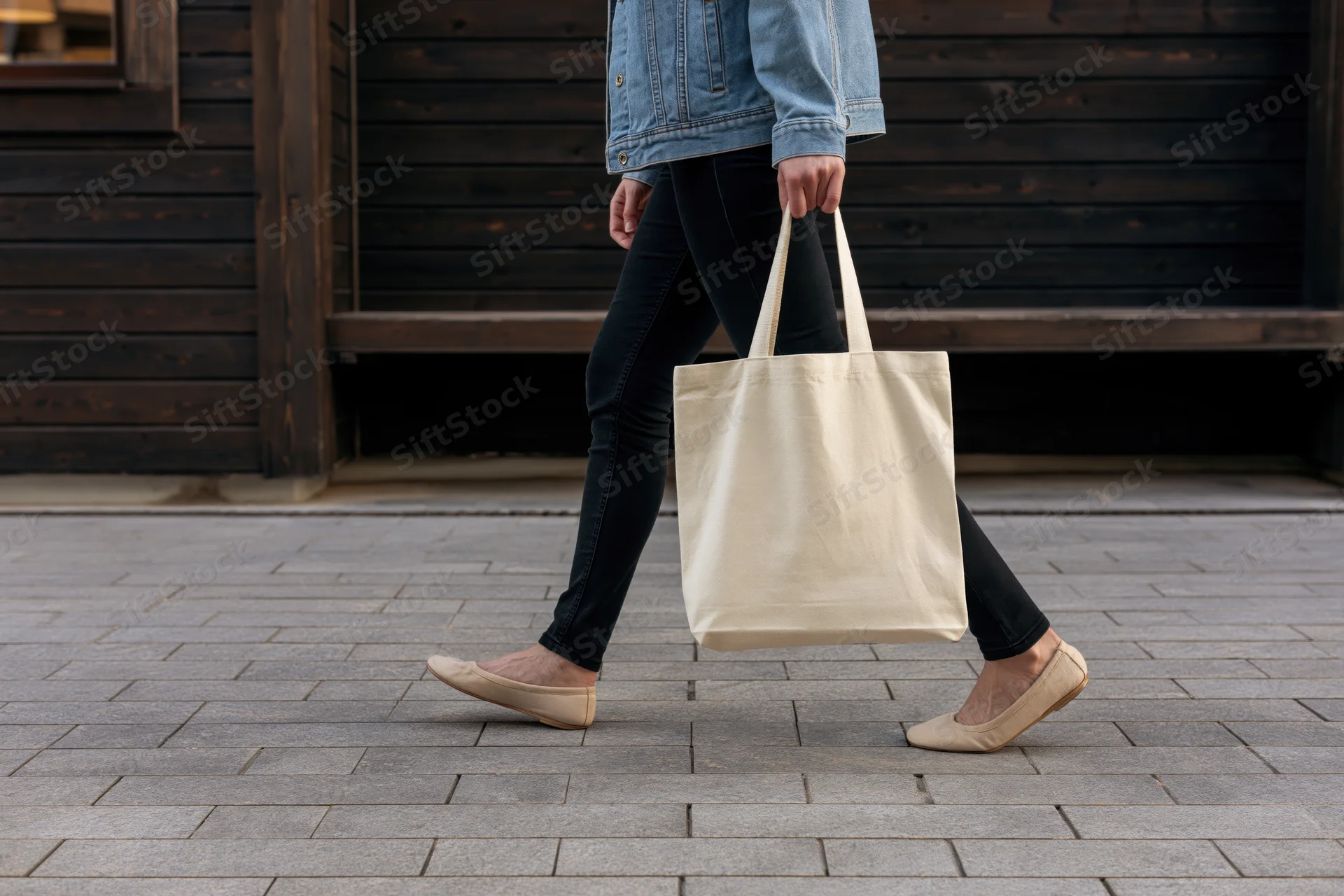 Woman walking on paved street carrying a plain canvas tote bag