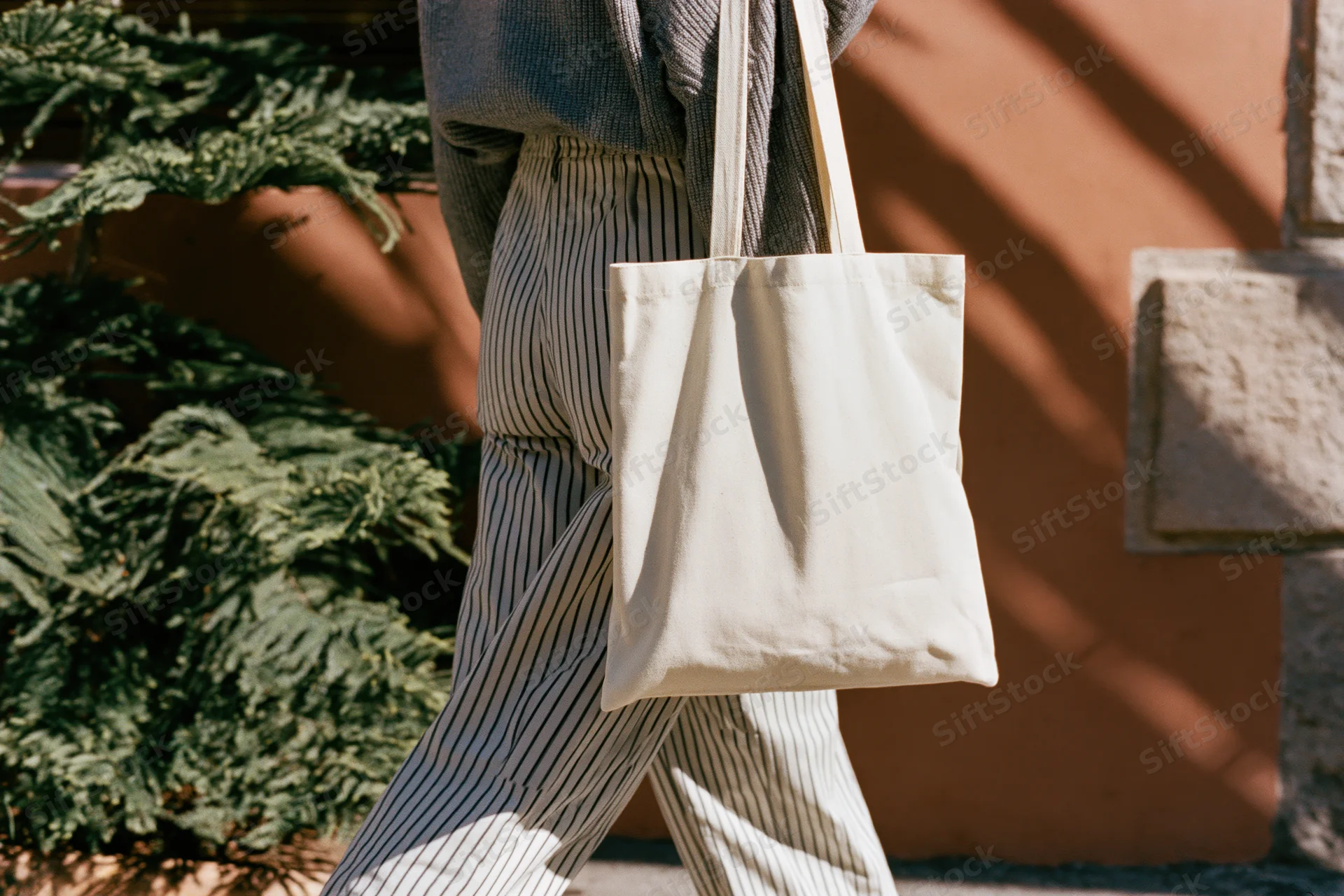 Woman walking outdoors carrying a plain cream cotton tote bag