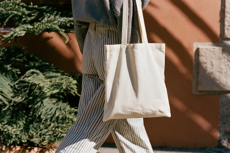 Woman walking outdoors carrying a plain cream cotton tote bag