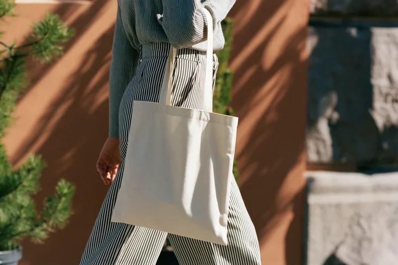 Woman walking outdoors carrying a plain cream cotton tote bag